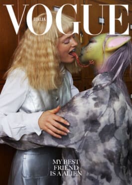 Femme blonde en veste argentée lèche la langue bleue d'un extraterrestre à peau verte et oreilles roses, dans un intérieur classique en bois. 